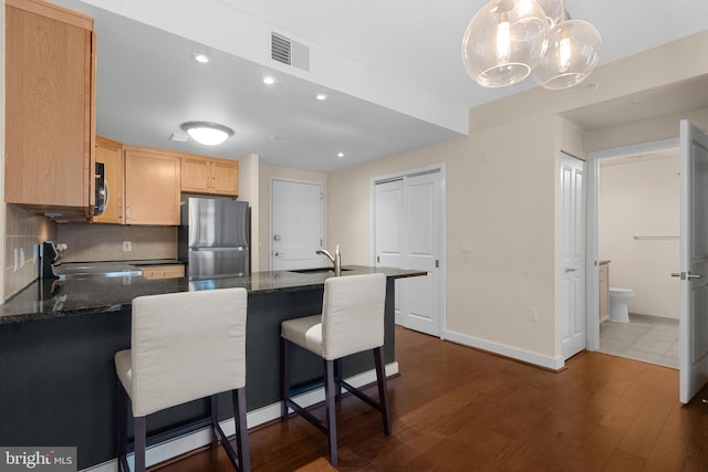 kitchen with stove, kitchen peninsula, pendant lighting, and stainless steel fridge