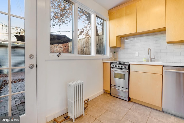 kitchen featuring radiator heating unit, sink, stainless steel appliances, tasteful backsplash, and light tile patterned flooring