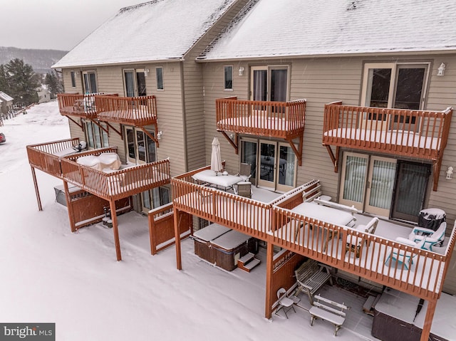 snow covered rear of property featuring a balcony and a hot tub