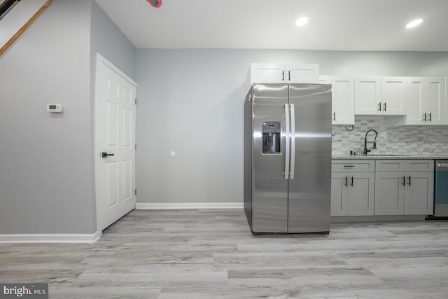 kitchen featuring decorative backsplash, light wood-type flooring, stainless steel appliances, sink, and white cabinetry