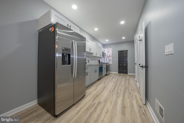 kitchen featuring sink, light hardwood / wood-style flooring, decorative backsplash, appliances with stainless steel finishes, and white cabinetry