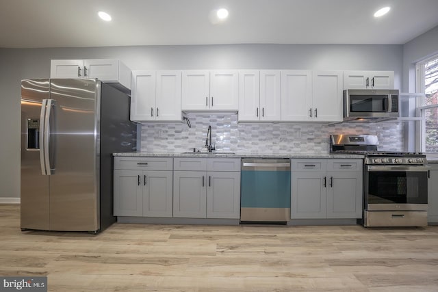 kitchen with light stone countertops, light wood-type flooring, stainless steel appliances, and sink