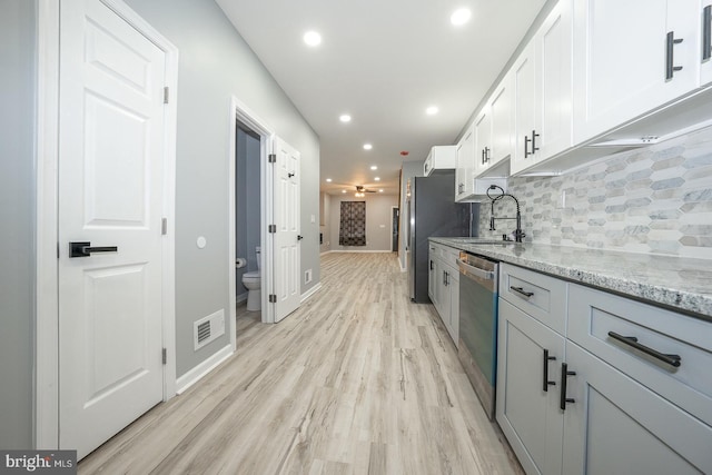 kitchen with sink, stainless steel appliances, light stone counters, white cabinets, and light wood-type flooring