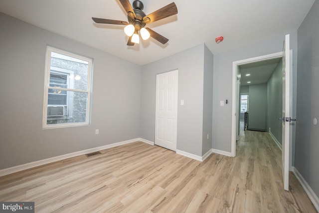 unfurnished bedroom with ceiling fan, light hardwood / wood-style floors, a closet, and multiple windows