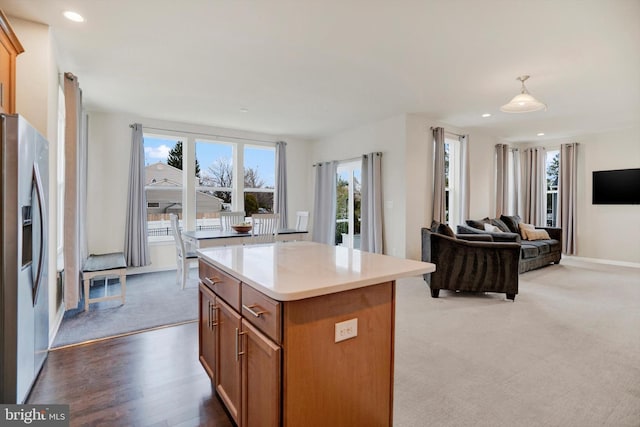 kitchen featuring stainless steel refrigerator with ice dispenser, a center island, decorative light fixtures, and light colored carpet