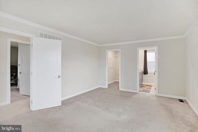 unfurnished bedroom with a spacious closet, crown molding, ensuite bathroom, light colored carpet, and a closet