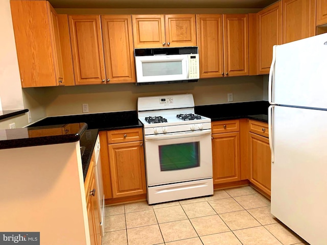 kitchen with light tile patterned flooring, white appliances, and dark stone counters