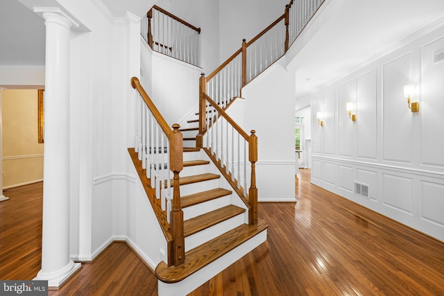 stairs with decorative columns, ornamental molding, and hardwood / wood-style flooring