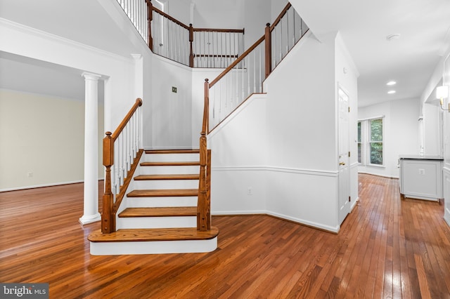 stairway with ornate columns, crown molding, and hardwood / wood-style flooring