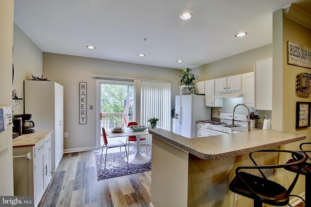 kitchen featuring white appliances, white cabinets, kitchen peninsula, a kitchen bar, and wood-type flooring