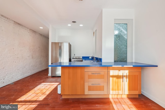 kitchen featuring kitchen peninsula, stainless steel refrigerator, dark wood-type flooring, and brick wall