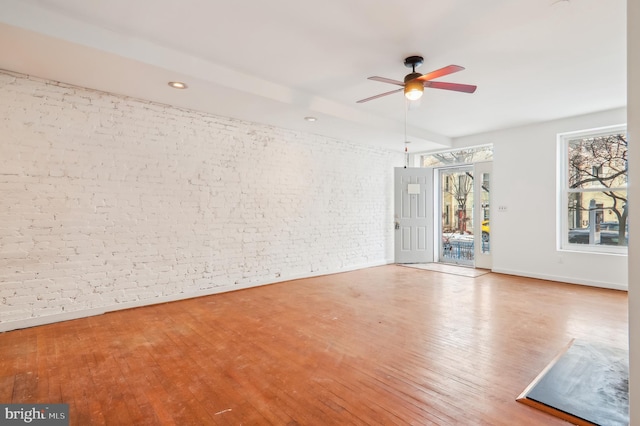 empty room with light wood-type flooring, ceiling fan, and brick wall