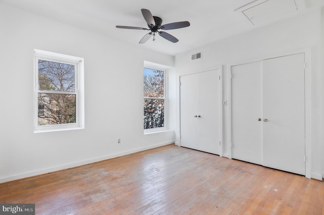 unfurnished bedroom with ceiling fan, light hardwood / wood-style flooring, and multiple closets