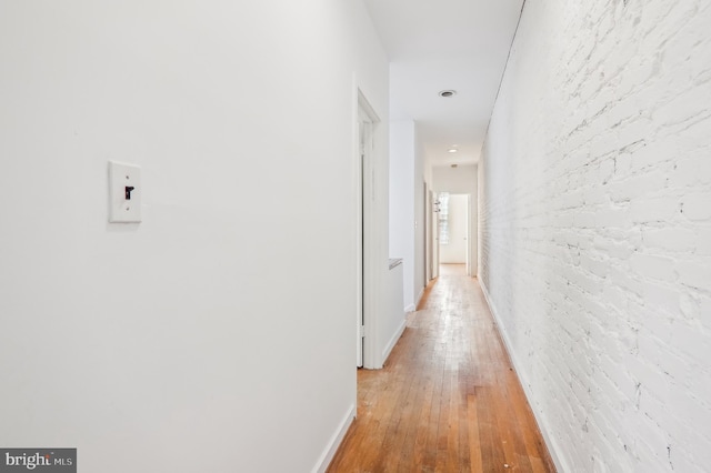 corridor featuring light hardwood / wood-style flooring and brick wall