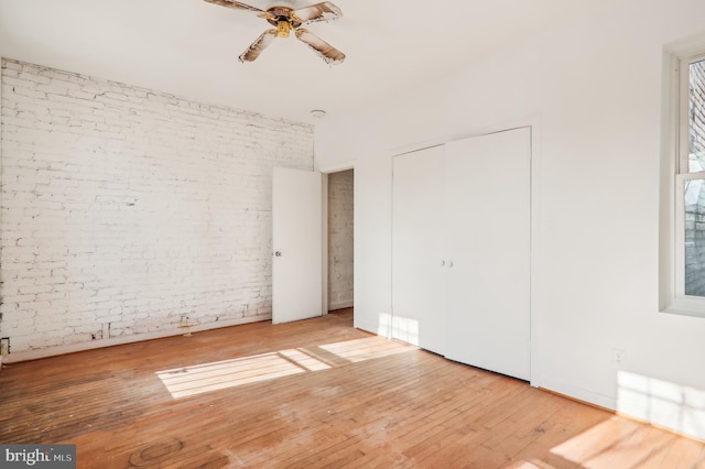 unfurnished bedroom featuring ceiling fan, brick wall, and wood-type flooring