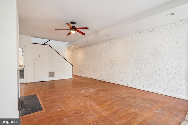 unfurnished living room with wood-type flooring, ceiling fan, and brick wall