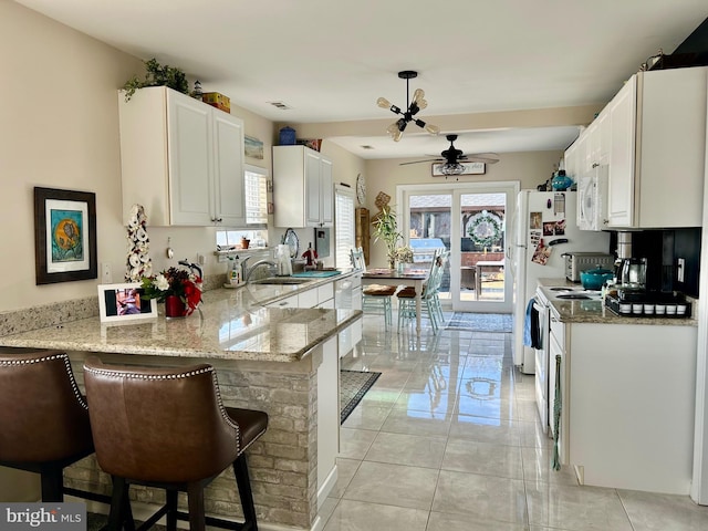 kitchen with a kitchen bar, kitchen peninsula, light stone countertops, and white cabinets