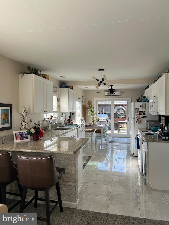 kitchen featuring white cabinetry, light stone countertops, kitchen peninsula, white appliances, and a breakfast bar