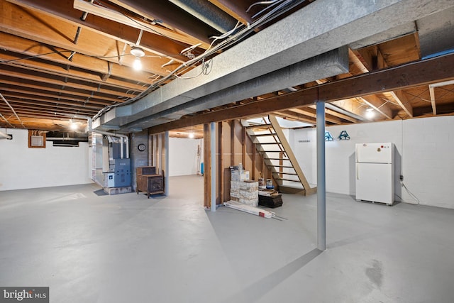 basement featuring white refrigerator and heating unit