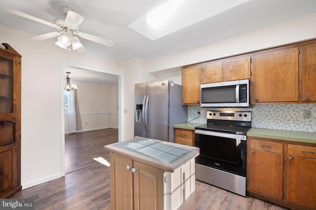 kitchen featuring ceiling fan with notable chandelier, tasteful backsplash, stainless steel appliances, and light hardwood / wood-style flooring