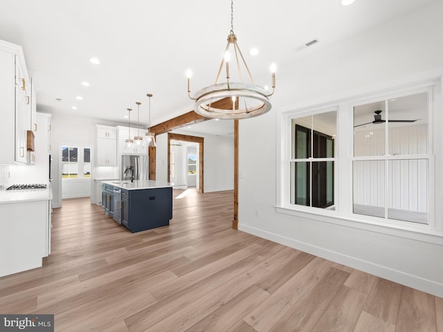 kitchen featuring blue cabinetry, pendant lighting, light wood-type flooring, and a center island with sink