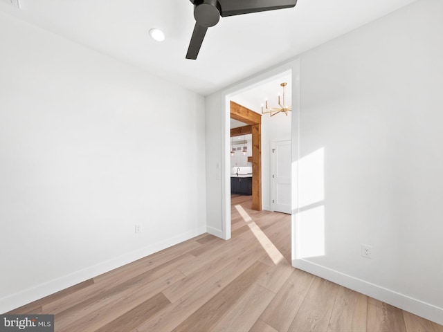 empty room with ceiling fan with notable chandelier and light hardwood / wood-style flooring