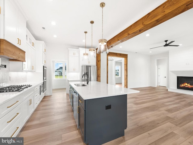 kitchen with a large island with sink, hanging light fixtures, appliances with stainless steel finishes, light hardwood / wood-style floors, and white cabinetry