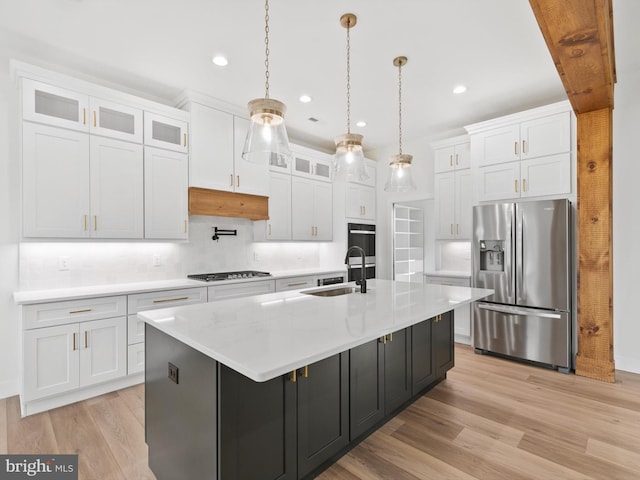 kitchen featuring white cabinets, a center island with sink, hanging light fixtures, appliances with stainless steel finishes, and light hardwood / wood-style floors