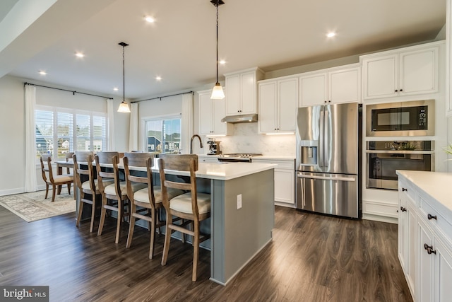 kitchen featuring appliances with stainless steel finishes, dark wood-type flooring, pendant lighting, a breakfast bar area, and an island with sink