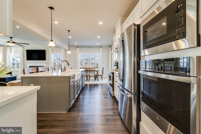 kitchen with a kitchen island with sink, hanging light fixtures, dark hardwood / wood-style floors, appliances with stainless steel finishes, and white cabinetry