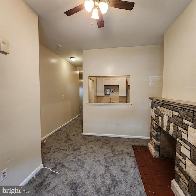 living room featuring a stone fireplace, ceiling fan, sink, and dark colored carpet