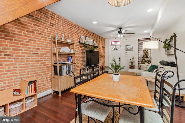 dining room featuring dark hardwood / wood-style floors, ceiling fan, and brick wall