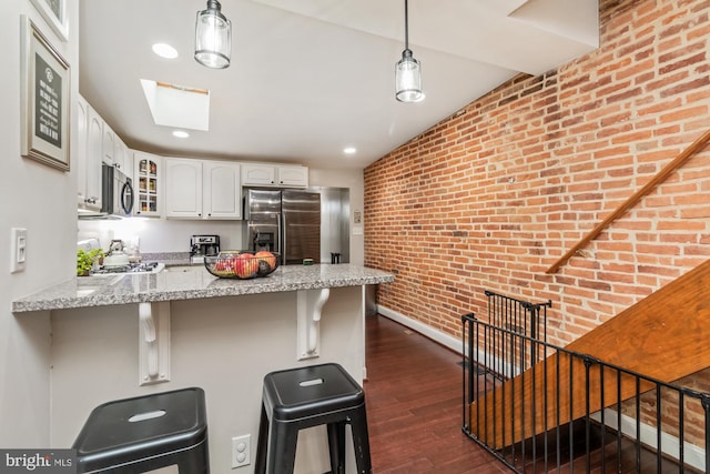 kitchen featuring stainless steel appliances, kitchen peninsula, a breakfast bar, and brick wall