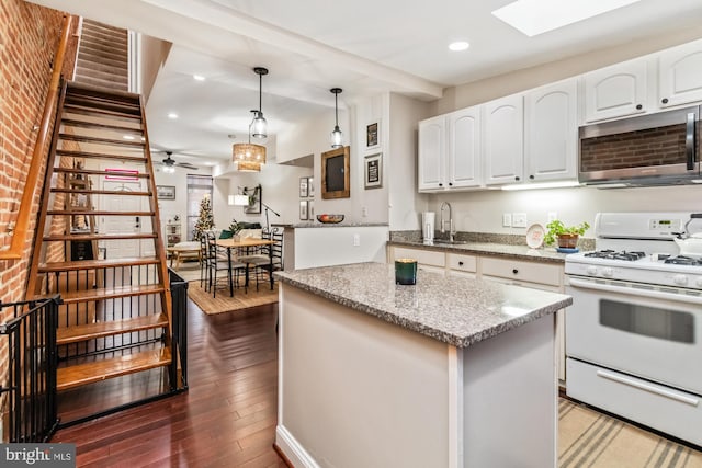 kitchen featuring pendant lighting, light stone counters, white cabinetry, and gas range gas stove