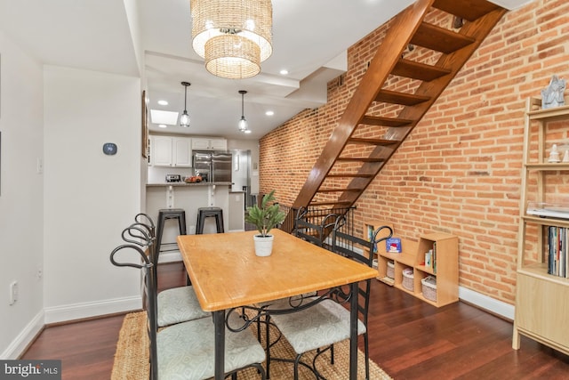 dining space featuring dark hardwood / wood-style flooring, brick wall, and a chandelier