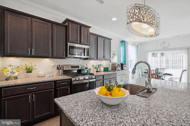 kitchen featuring dark brown cabinetry, sink, light stone counters, appliances with stainless steel finishes, and pendant lighting