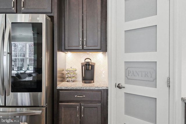 kitchen featuring light stone counters, backsplash, dark brown cabinets, and stainless steel refrigerator