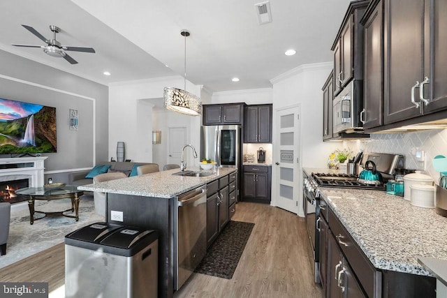 kitchen featuring sink, hanging light fixtures, appliances with stainless steel finishes, an island with sink, and backsplash