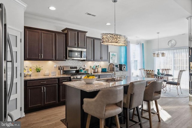 kitchen featuring appliances with stainless steel finishes, decorative light fixtures, light stone countertops, and an island with sink