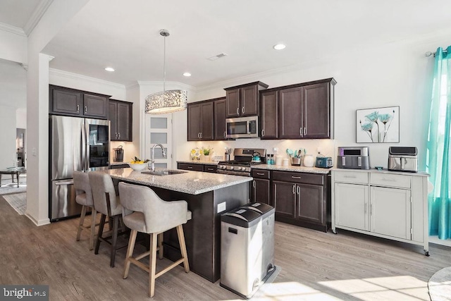 kitchen with pendant lighting, sink, light hardwood / wood-style flooring, stainless steel appliances, and an island with sink