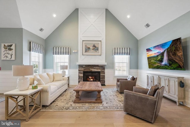 living room with high vaulted ceiling, a stone fireplace, and light hardwood / wood-style floors