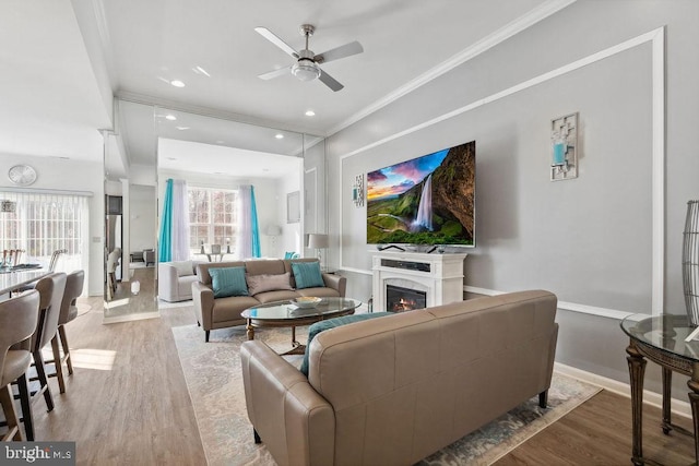 living room with a premium fireplace, ornamental molding, ceiling fan, and light hardwood / wood-style floors