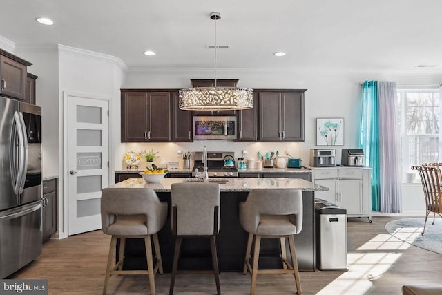 kitchen featuring appliances with stainless steel finishes, light stone counters, light hardwood / wood-style floors, a center island with sink, and decorative light fixtures