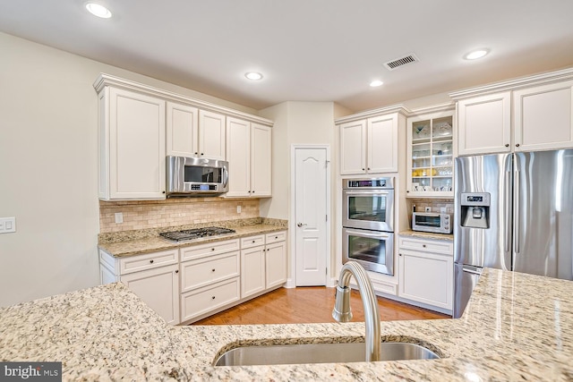 kitchen with appliances with stainless steel finishes, tasteful backsplash, sink, white cabinets, and light hardwood / wood-style floors