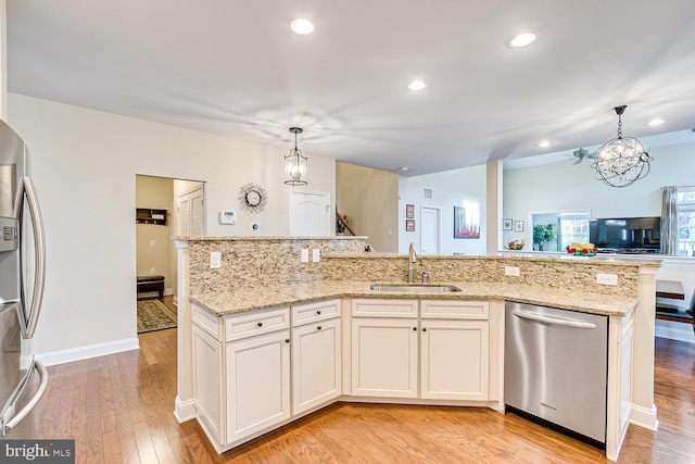 kitchen with appliances with stainless steel finishes, light stone counters, sink, light hardwood / wood-style flooring, and hanging light fixtures