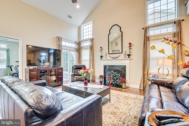 living room with a high end fireplace, hardwood / wood-style floors, high vaulted ceiling, and a wealth of natural light