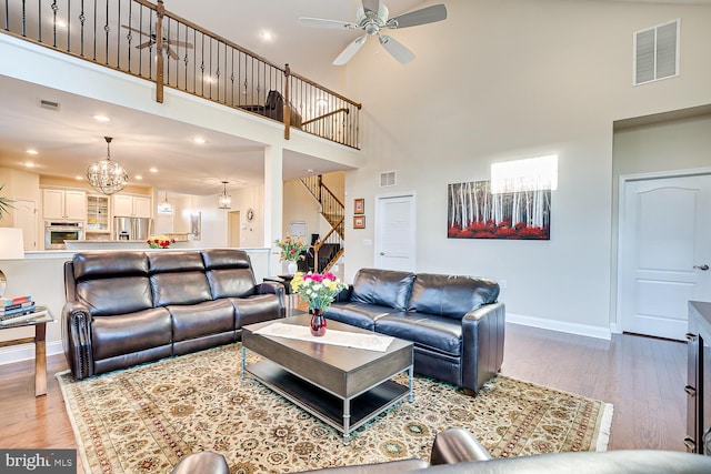 living room with ceiling fan with notable chandelier, light hardwood / wood-style floors, and high vaulted ceiling