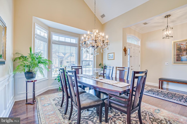 dining room with hardwood / wood-style flooring, ornamental molding, high vaulted ceiling, and an inviting chandelier