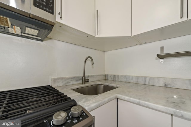 kitchen with black range oven, white cabinetry, and sink