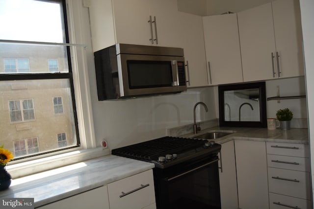 kitchen with white cabinets, sink, and black range